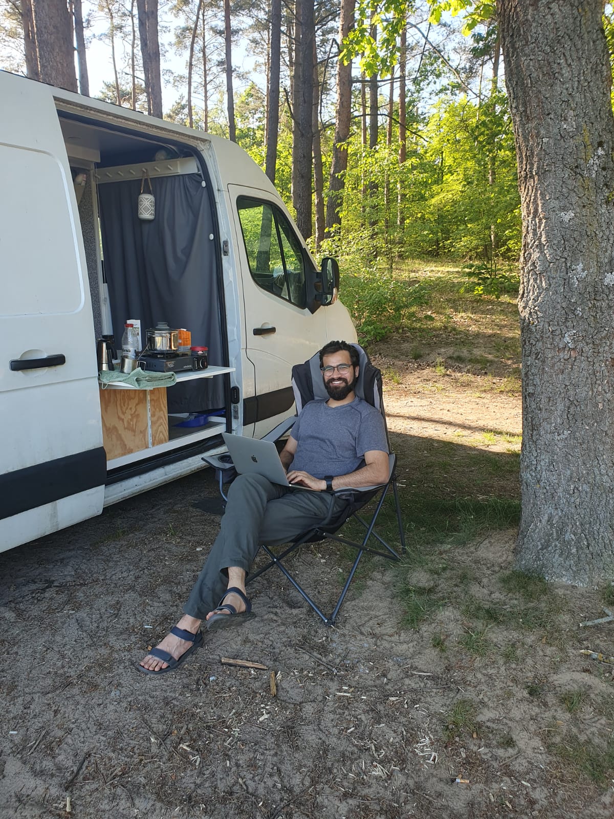 Working from a folding chair next to a campervan parked in a pine forest.