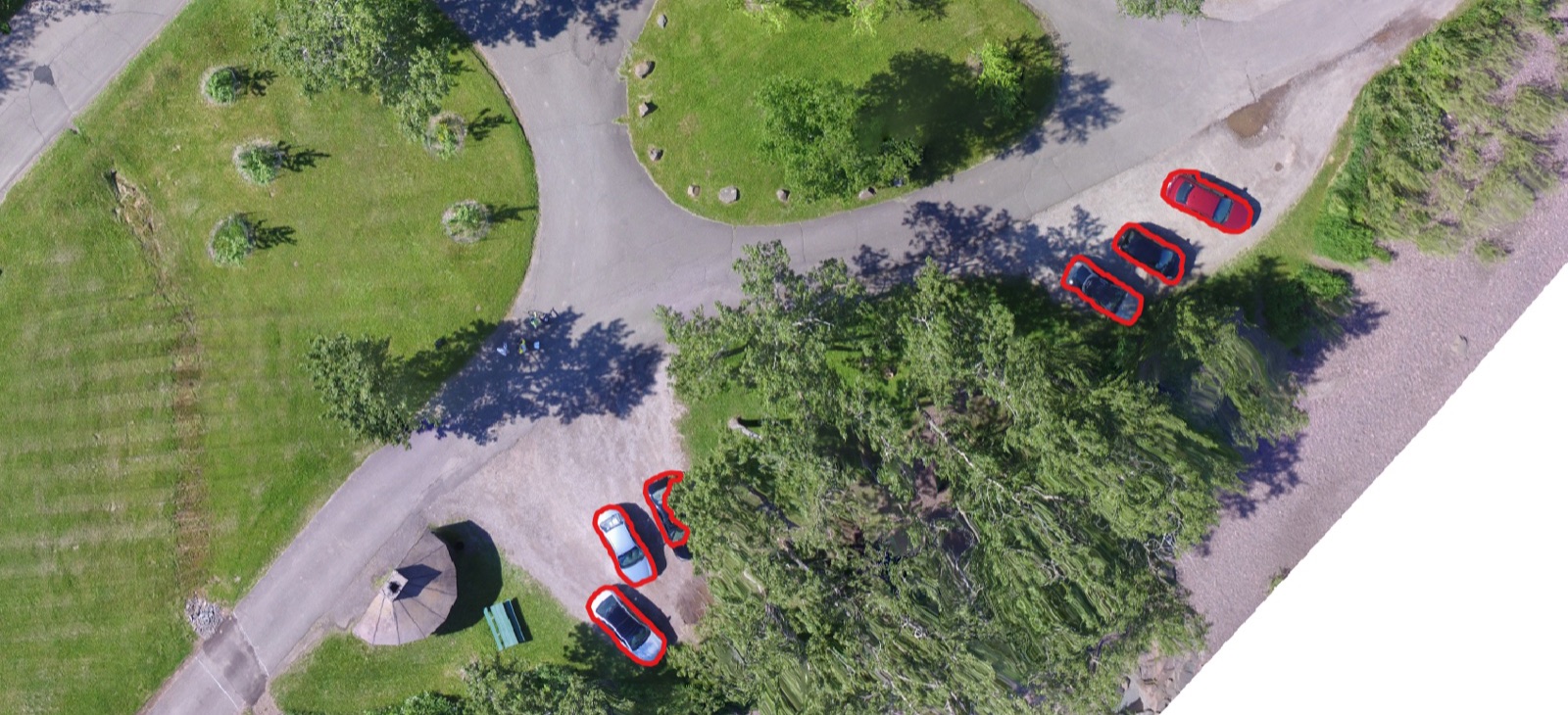 A drone orthomosaic of a park, with every car automatically outlined in red by the segmentation model.
