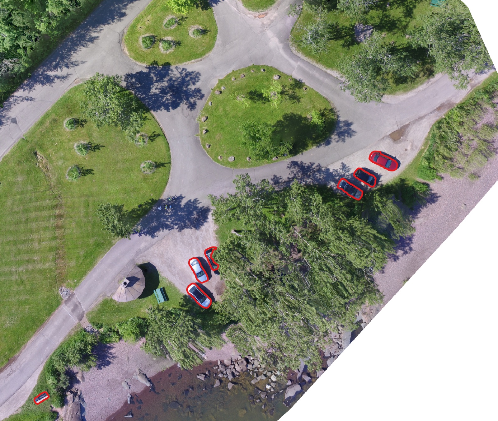 A drone orthomosaic of a park and shoreline, with every car outlined in red by the segmentation model.